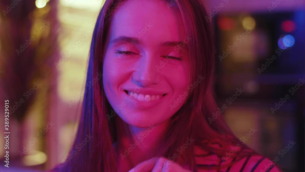 Face charming young woman look at camera smiling feel happy sitting on sofa at neon light. Poses at home relax attractive. Close up. Portrait. Slow motion Face charming young woman look at camera smiling feel happy sitting on sofa at neon light. Poses at home relax attractive. Close up. Portrait. Slow motion