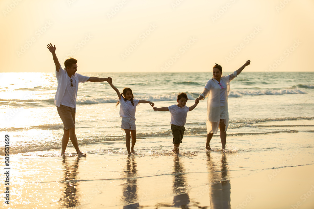 Happy Asian Family parents with two child boy and girl holding hands and walking together on the beach at summer sunset. Father, mother and kids enjoy and having fun in outdoor holiday vacation.