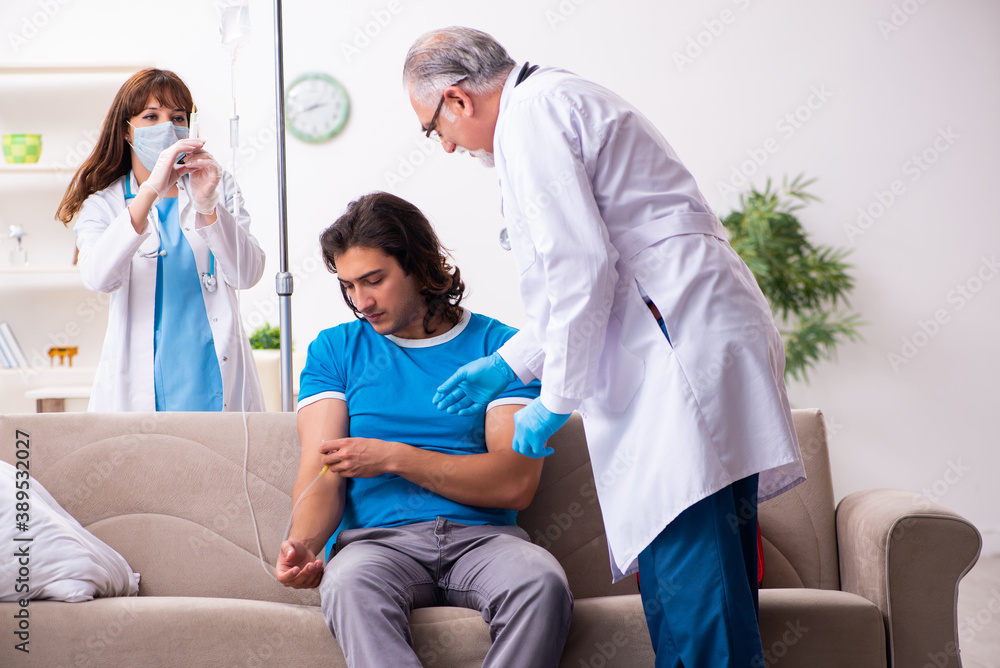 Obraz premium Two doctors visiting sick young man at home
