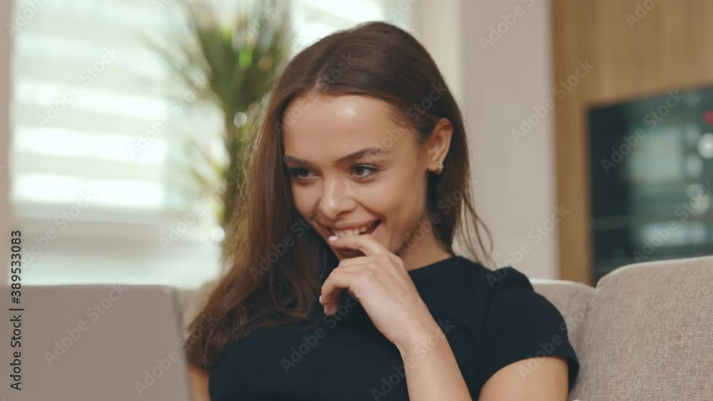 Attractive young woman relaxing on sofa use laptop chatting with friends online in social network. Feel happy smiling. In modern room at home. Close up. Slow motion