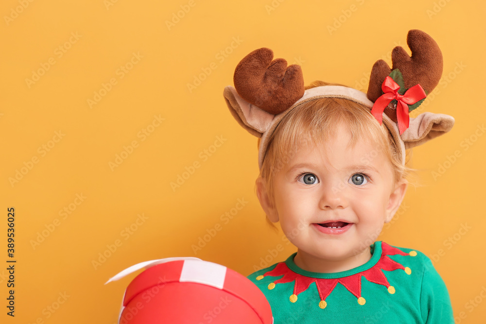 Cute little baby in elf's costume and with deer horns on color background