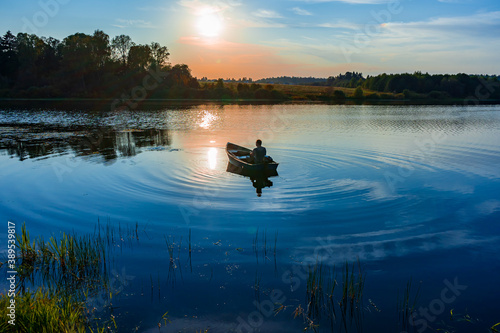 Mature caucasian man fishing in a small boat with a motor at sunset on the lake