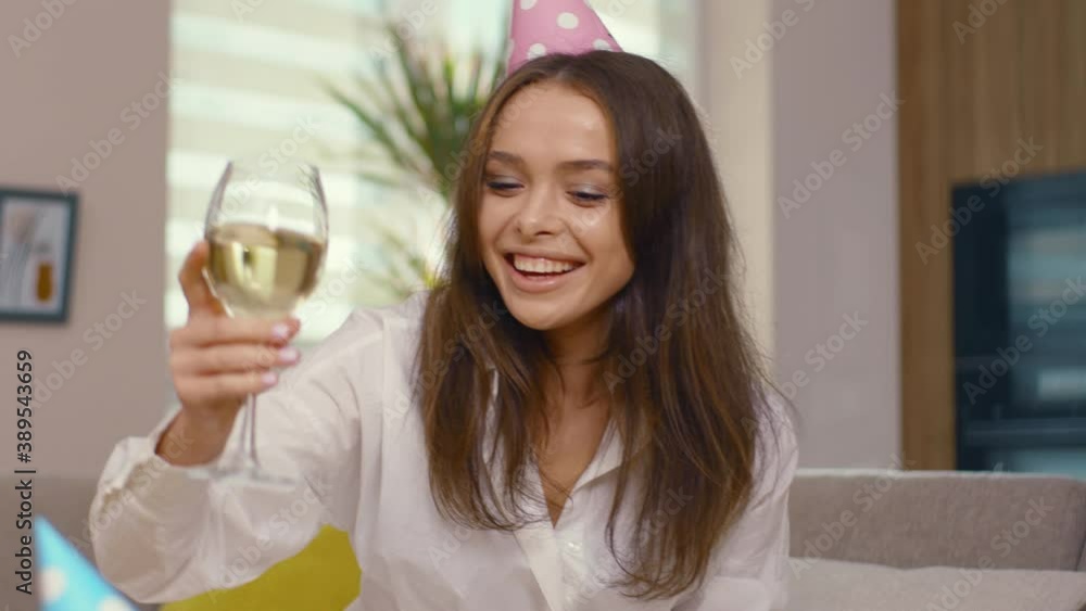 Caucasian young woman freelancer spending holiday party home birthday celebrating wearing festive cap holding glass of alcohol videochatting with colleagues on laptop. Self-isolation, social distance. Caucasian young woman freelancer spending holiday party home birthday celebrating wearing festive cap holding glass of alcohol videochatting with colleagues on laptop. Self-isolation, social distance.