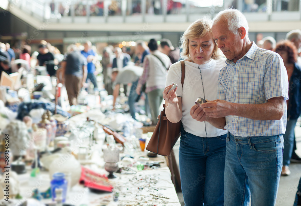Elderly man and woman consider things in flea market. High quality photo