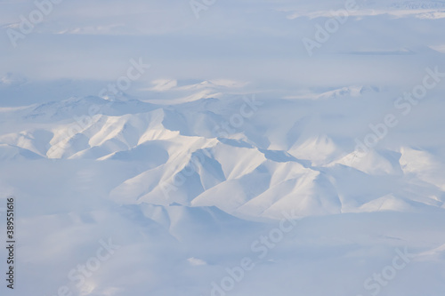 Aerial view of snow-capped mountains and clouds. Winter snowy mountain landscape. Kolyma Mountains on the border of Kamchatka Territory and Magadan Region, Siberia, Far East Russia. Great background.