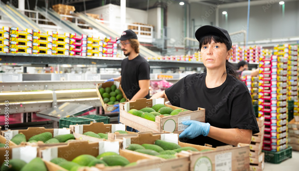 Woman worker in uniform keeping avocado box in hands at warehouse.