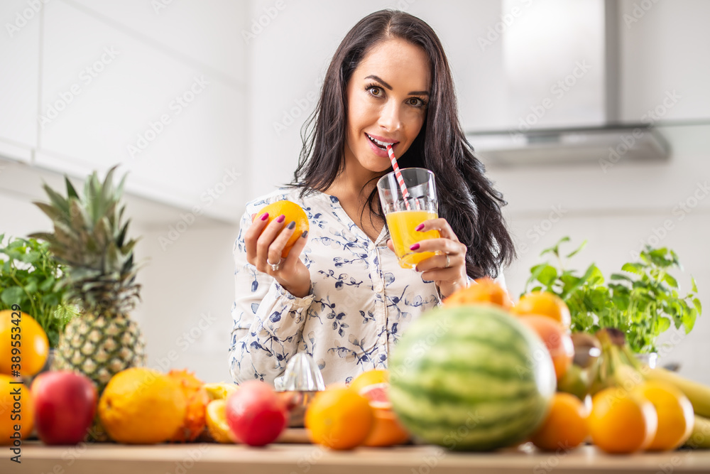 Girl sips a freshly squeezed orange juice with a paper straw surrounded by assortment of fruit Girl sips a freshly squeezed orange juice with a paper straw surrounded by assortment of fruit