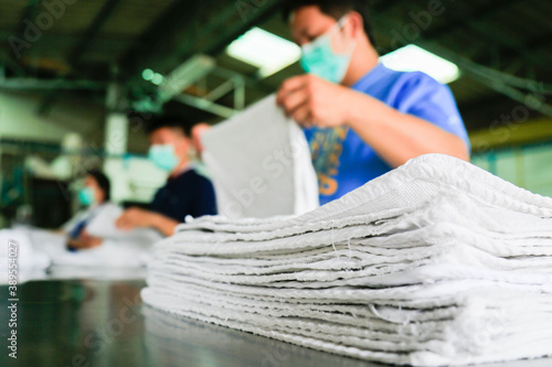 Laundry staffs wearing a mask are folding towels. Shot taken in the factory. Focus on towels.