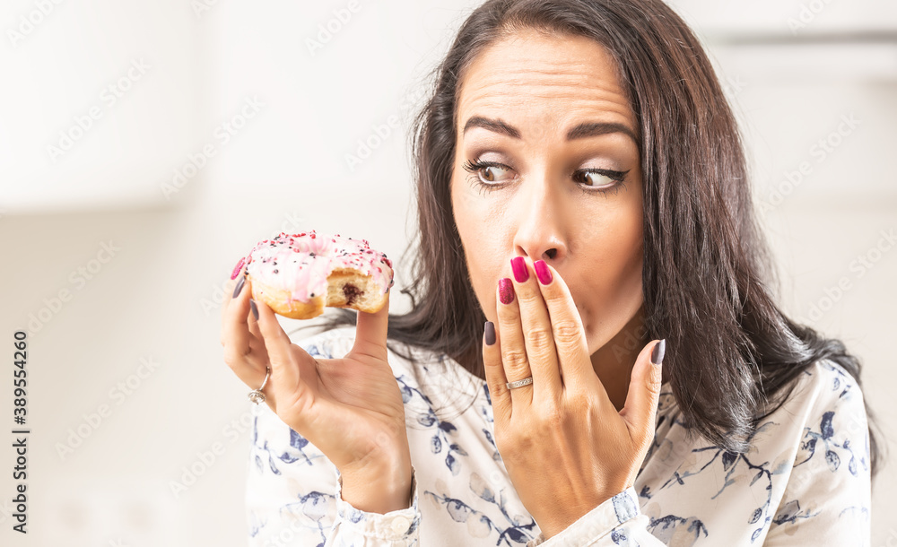 Oops expression on a face of a woman who has bitten into a donut in her hand Oops expression on a face of a woman who has bitten into a donut in her hand