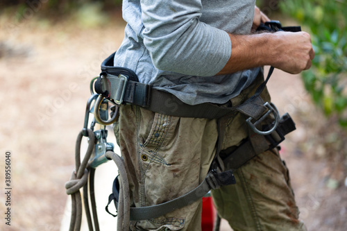 Cropped view of man with the chainsaw use safety harness and safety line working on a garden. Lumberjack with chainsaw against nature background. Concept building, contractor, repair, lumberjack.