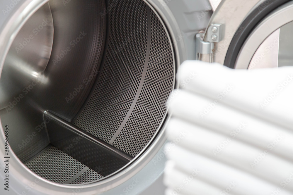 Stack of bed sheets in front of industrial laundry washing machine. Metal tub is inside. Focused on washing machines. Shot taken in the factory. Stack of bed sheets in front of industrial laundry washing machine. Metal tub is inside. Focused on washing machines. Shot taken in the factory.