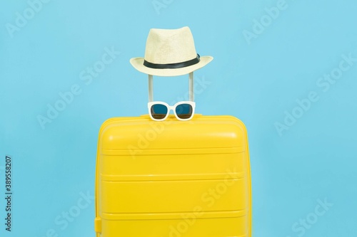 Summer time - Yellow suitcase or luggage with hat and sunglasses on pastel blue background minimal creative travel concept Holiday Adventure Trip.