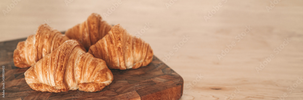 Fresh baked croissants on wooden board banner background. French pastries from bakery.