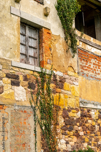 Old window with wooden shutters on a cracked stone and brick wall with ivy