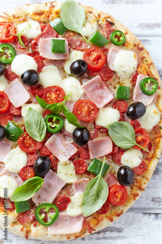 Pizza with ham, mozzarella cheese, cherry tomatoes, green and jalapeno pepper, black olives and fresh basil. Bright background. Top view. Close up.	