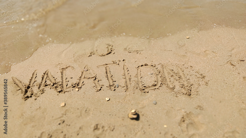 Fototapeta premium Text Vacation written in the sand of sea beach