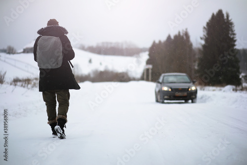 A man in winter clothes on the street. Tourists travel through the snowy country. On the way, walk and hitchhike.