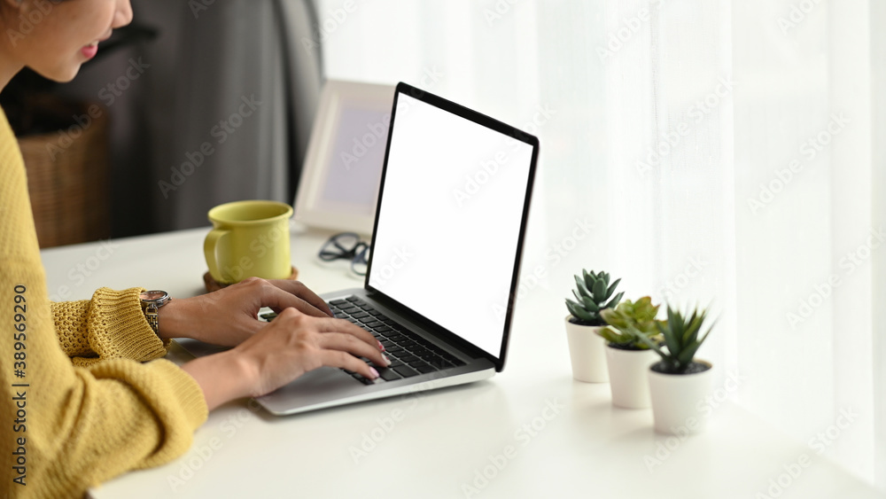 Cropped shot of a young female in yellow sweater typing on keyboard of laptop while sitting in front of blank screen laptop in office. Cropped shot of a young female in yellow sweater typing on keyboard of laptop while sitting in front of blank screen laptop in office.
