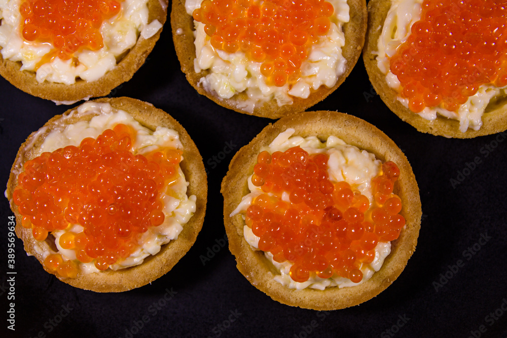 Tartlets with red caviar on a black plate. Festive food. Top view
