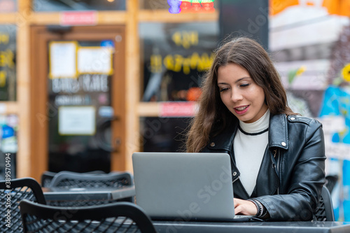 Portrait of a happy young woman relaxing in outdoor cafe and using a laptop