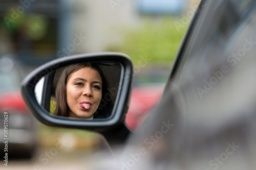 teenager driver looks in the rearview mirror of the car and shows her tongue