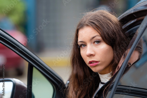 young woman sits in a car with an open door and looks back, close-up portrait