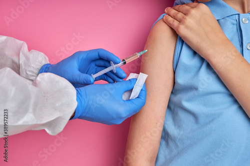Fototapeta Naklejka Na Ścianę i Meble -  close up of doctor hand using syringe to make vaccine injection to cropped child boy patient, isolated on pink background