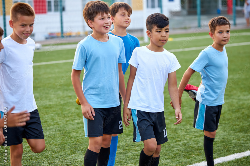 Obraz premium group of caucasian kid boys stretching legs before football game in stadium, they are in special sportive uniform, engaged in sport and healthy lifestyle from childhood