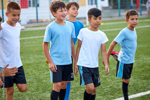 group of caucasian kid boys stretching legs before football game in stadium, they are in special sportive uniform, engaged in sport and healthy lifestyle from childhood © Roman