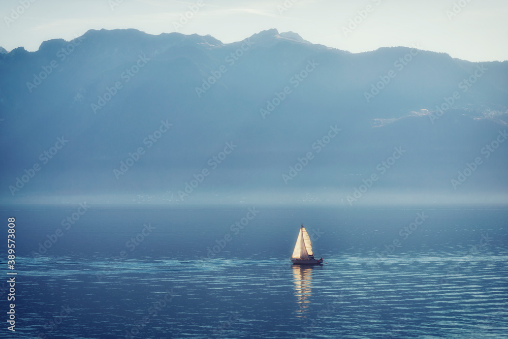 Sailing boat cutting through a tranquil misty mountain lake.