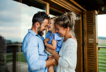 Family with small daughter standing on patio of wooden cabin, holiday in nature concept.