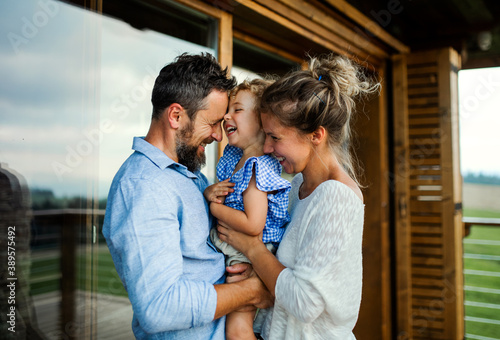 Family with small daughter standing on patio of wooden cabin, holiday in nature concept. photo