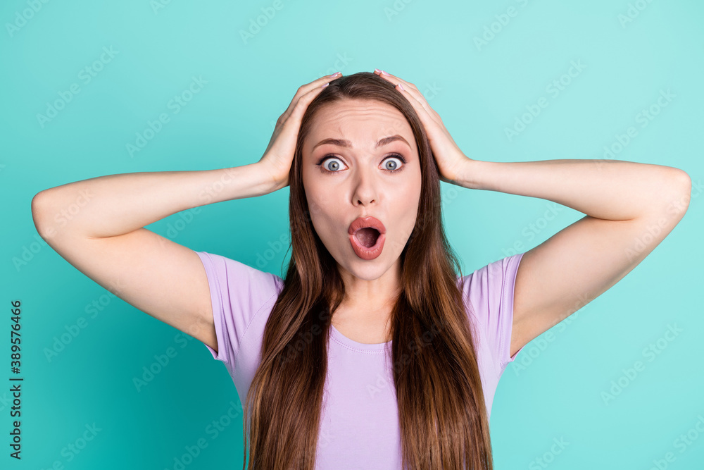 Photo portrait of troubled woman keeping head with hands staring with opened mouth isolated on bright teal color background Photo portrait of troubled woman keeping head with hands staring with opened mouth isolated on bright teal color background