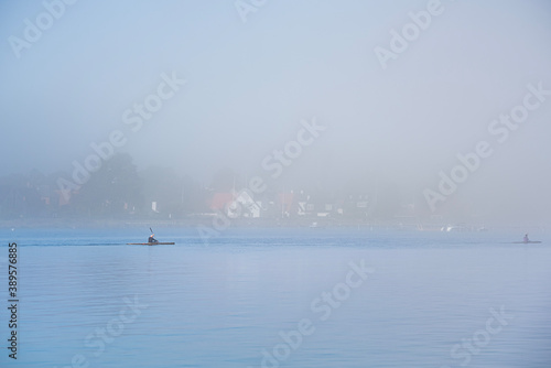 Stay fit rowing a canoe or kayak amidst the mist on a gloomy day. People keep fit kayaking amid tranquility on a still, calm Baltic sea as the coast is visible through the fog - Dragor Havn, Denmark © Roberto