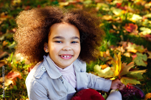 Cute Afro girl is smiling widely in the open air, having a picnic and enjoying an autumn day in the Park. Playing with leaves.