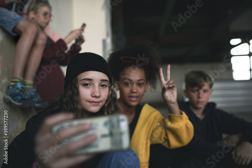 Group of teenagers gang sitting indoors in abandoned building, taking selfie with smartphone.