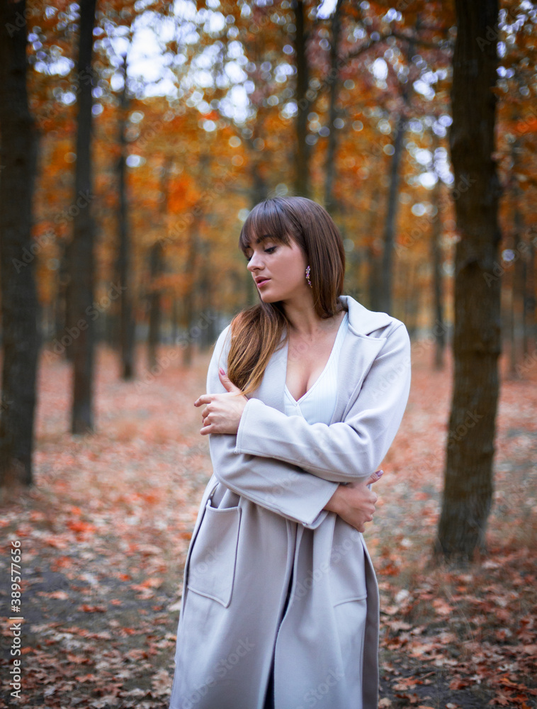 stylish young caucasian female with dark hair in the light coat in autumn park, trees with orange leaves stylish young caucasian female with dark hair in the light coat in autumn park, trees with orange leaves