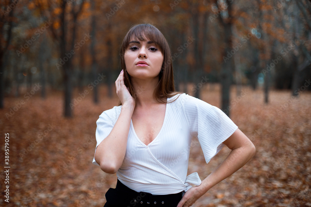 stylish young caucasian female with dark hair in the white blouse on the alley in autumn park, trees with orange leaves stylish young caucasian female with dark hair in the white blouse on the alley in autumn park, trees with orange leaves