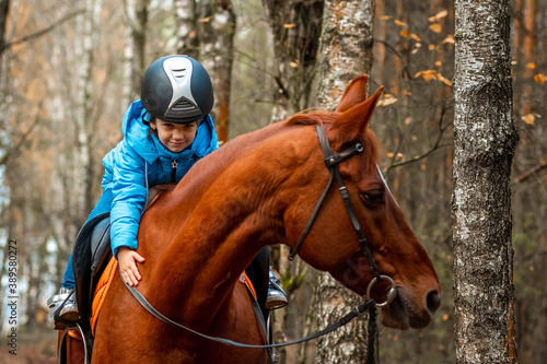 Little girl on an adult brown horse on the background of nature. Jockey, epodrome, horseback riding. © Aliaksandr Marko