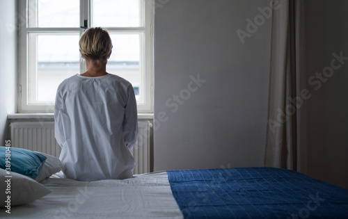 Rear view of woman patient sitting on bed in hospital feeling stressed, mental health and coronavirus concept. photo