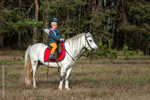 Little girl on a white pony on a background of nature. Jockey, hippodrome, horseback riding.