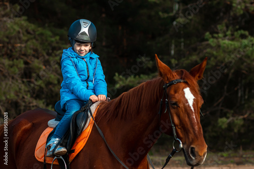 Little girl on an adult brown horse on the background of nature. Jockey, epodrome, horseback riding. © Aliaksandr Marko