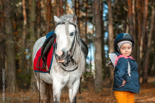 Little girl portrait, stands next to a white pony close-up on the background of nature. Jockey, epodrome, horseback riding © Aliaksandr Marko