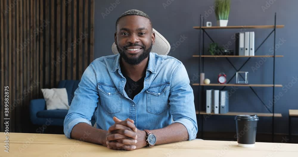 Portrait of Young Hipster African American Freelancer is smiling at the Camera. Front View of Young handsome Man is looking nice, cute. Contemporary People. Casual Lifestyle. Working Indoor. Portrait of Young Hipster African American Freelancer is smiling at the Camera. Front View of Young handsome Man is looking nice, cute. Contemporary People. Casual Lifestyle. Working Indoor.