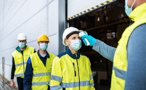 Group of workers with face mask in front of warehouse, coronavirus and temperature measuring concept.