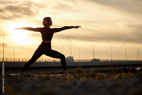 beautiful slim sporty woman in yoga pose outdoors in city, caucasian female is dressed in sportwears, has short hair, well shaped and flexible young woman trains alone.healthy lifestyle concept.