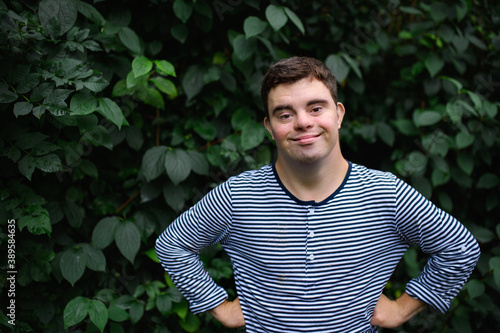 Portrait of down syndrome adult man standing outdoors at green background, looking at camera.