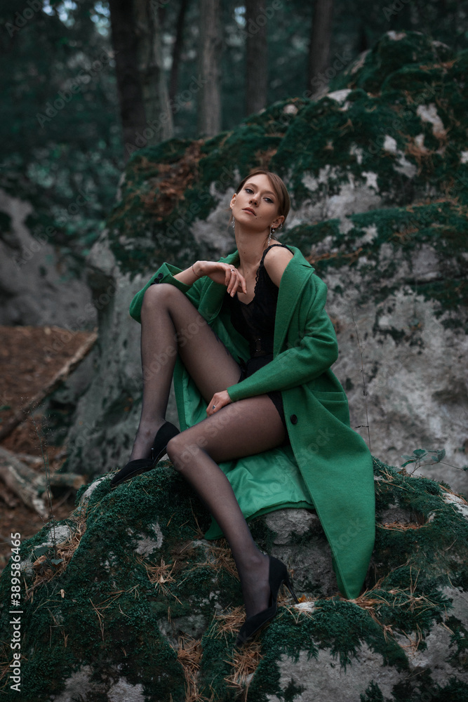 Fashionable young woman in green coat posing in a forest Fashionable young woman in green coat posing in a forest