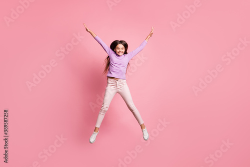 Full length photo of carefree kid girl jump up raise hands isolated over pastel color background