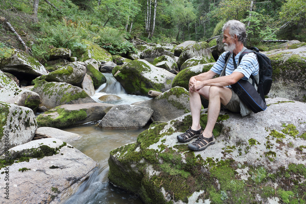 Man with a backpack sitting on a stone near a mountain river on a summer day, Belokurikha River, Altai Mountains Man with a backpack sitting on a stone near a mountain river on a summer day, Belokurikha River, Altai Mountains